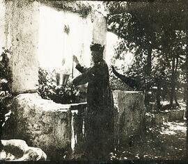 Málaga, retrato de un cura tocado con un bonete, sacando agua de un pozo en algúna finca de la vega. Fotógrafo desconocido.