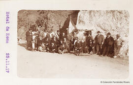 Málaga, retrato de un grupo de excursionistas con niños y un perro ante una "casa cueva" con una bandera en un lugar indeterminado. Fotógrafo desconocido.
