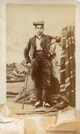 Retrato de un hombre con traje catalán y un bastón en un estudio con decorado. Fotógrafo desconocido.