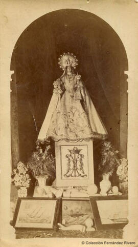 Imagen de una Virgen del Carmen, coronada, con exvotos a sus pies. Fotógrafo desconocido.